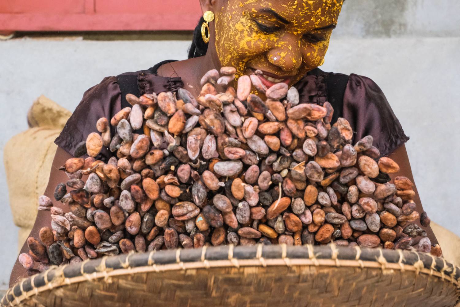 A woman with yellow stains throws cocoa beans into the air with a bowl.